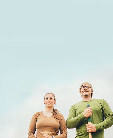 Marie und Nils Schneider stehen vor hellblauem Himmel nebeneinander und blicken in die Weite.