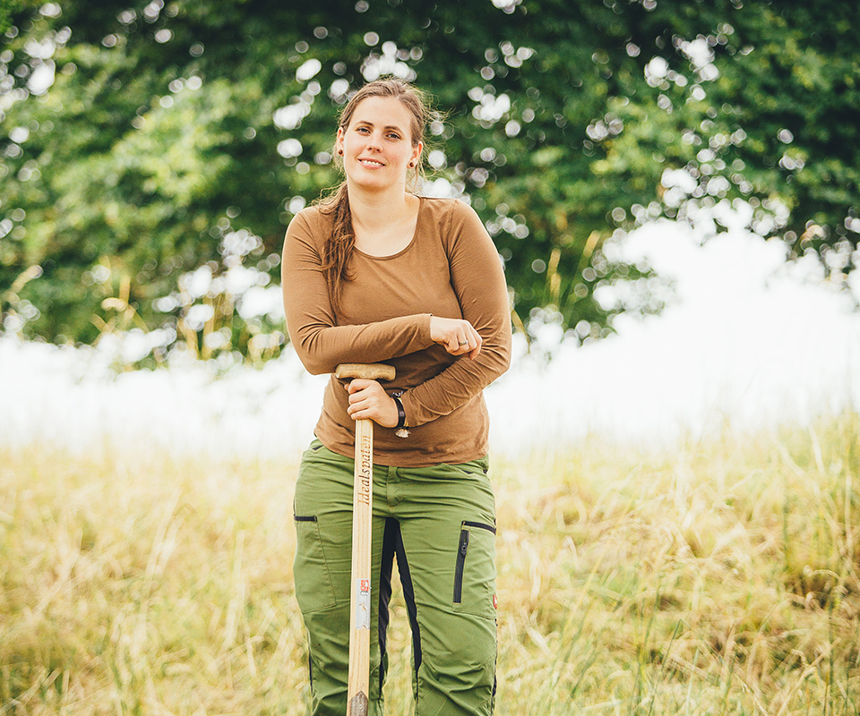 Portrait von Marie Schneider, die auf einen Spaten aufgestützt steht.