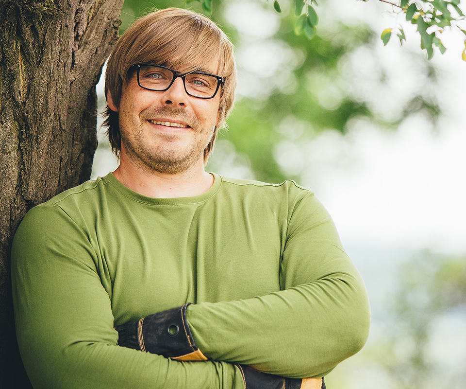 Portrait von Nils Schneider. Er steht angelehnt an einem Baum.